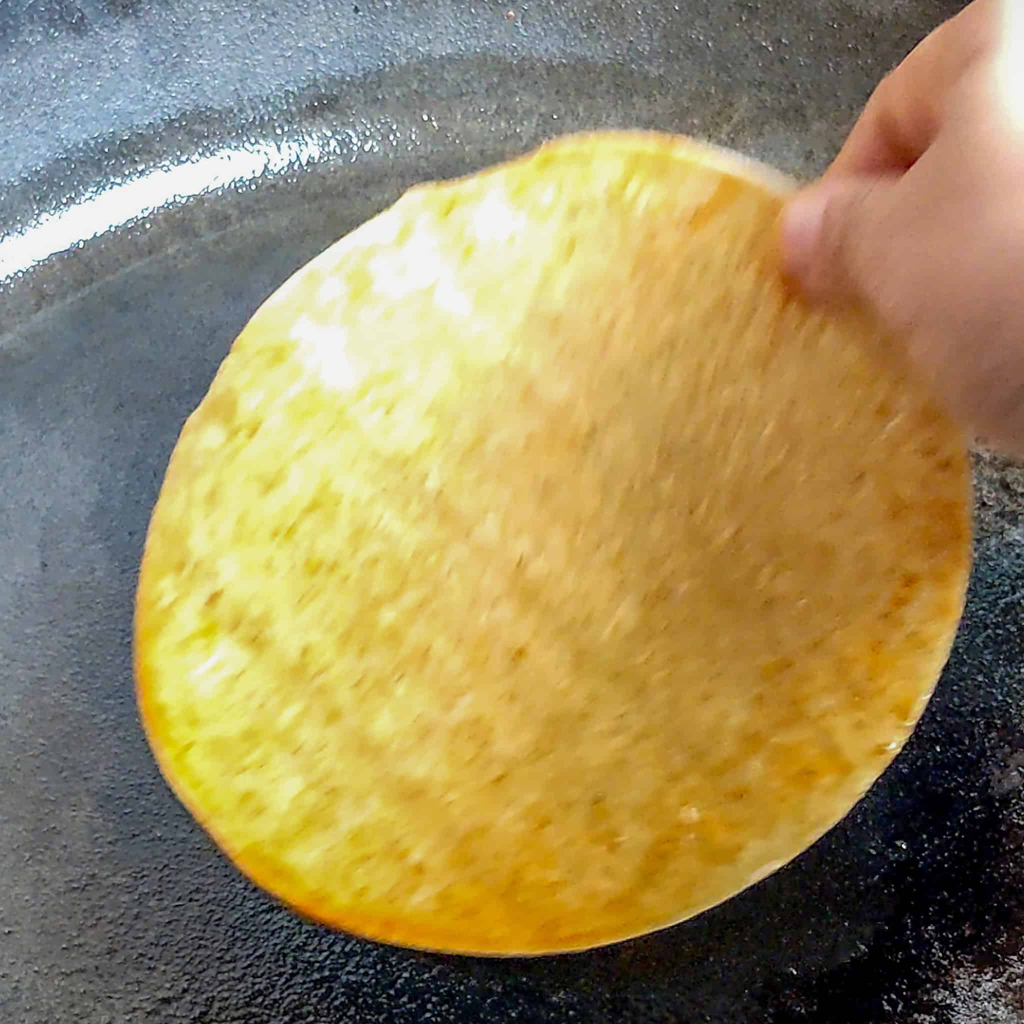 birria consume coated corn tortilla being added to cast Iron skillet.